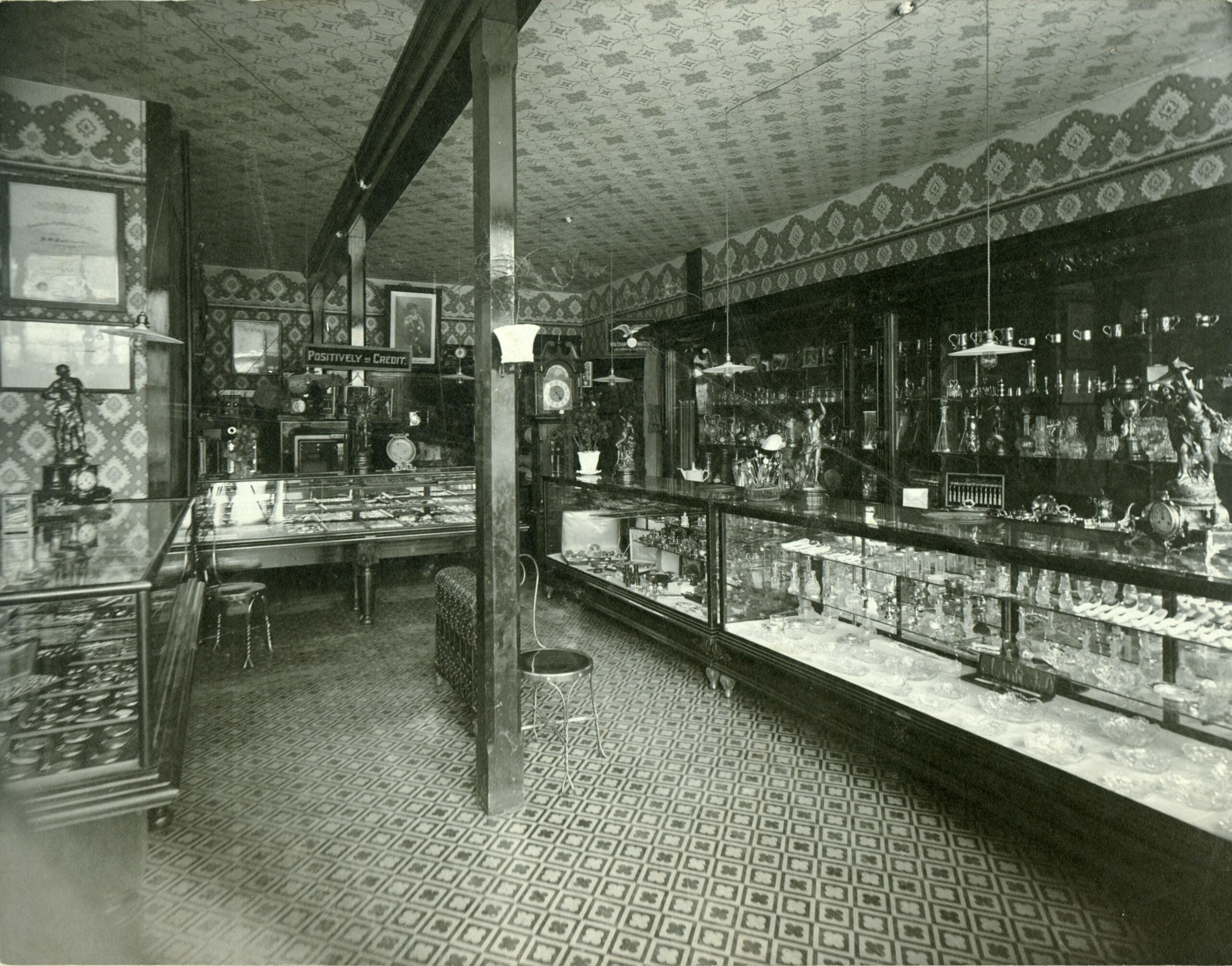 Inside lowly lit early 1900s shop with wraparound glass cases filled with jewelry