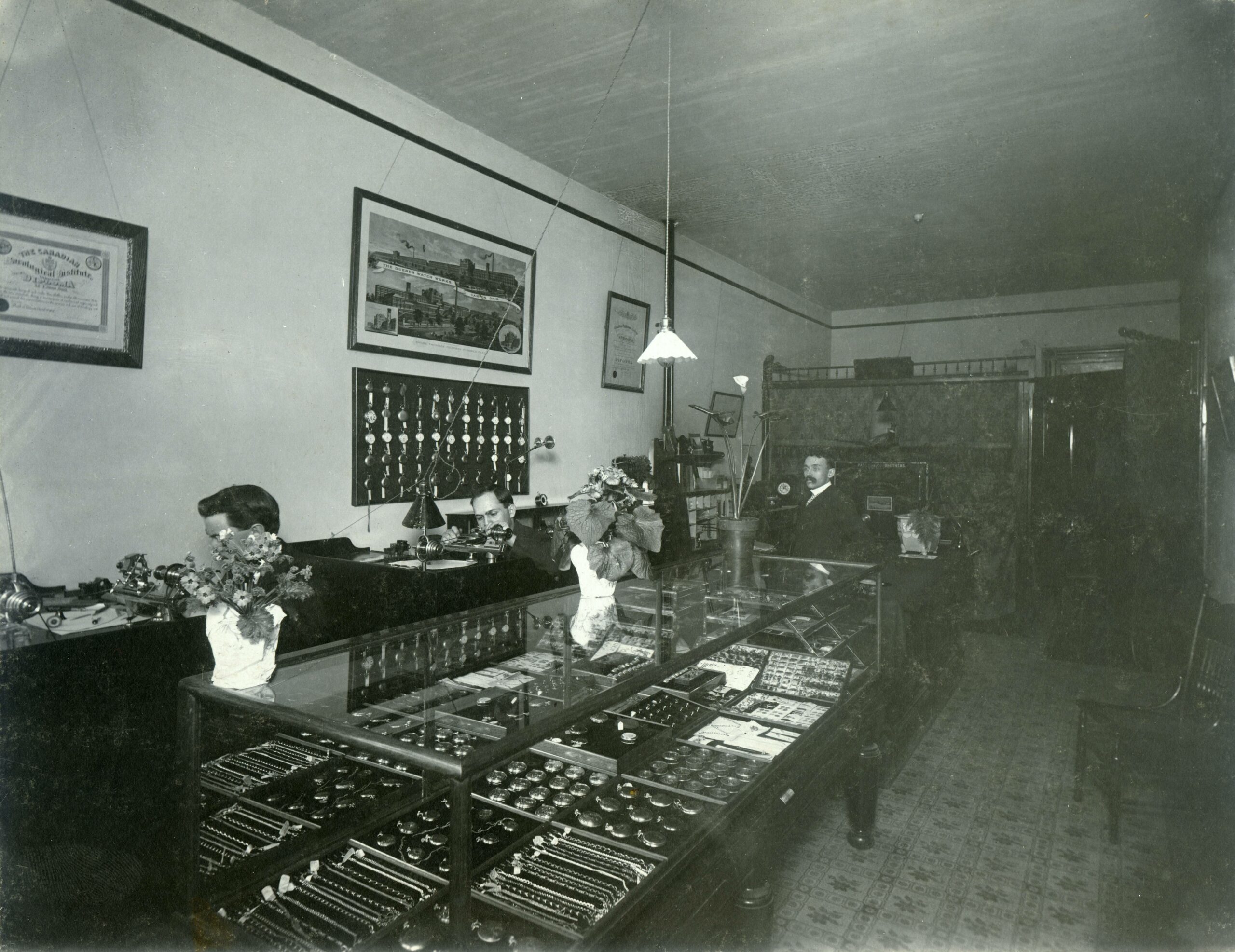 Inside lowly lit early 1900s shop with c a glass case on the left filled with jewelry