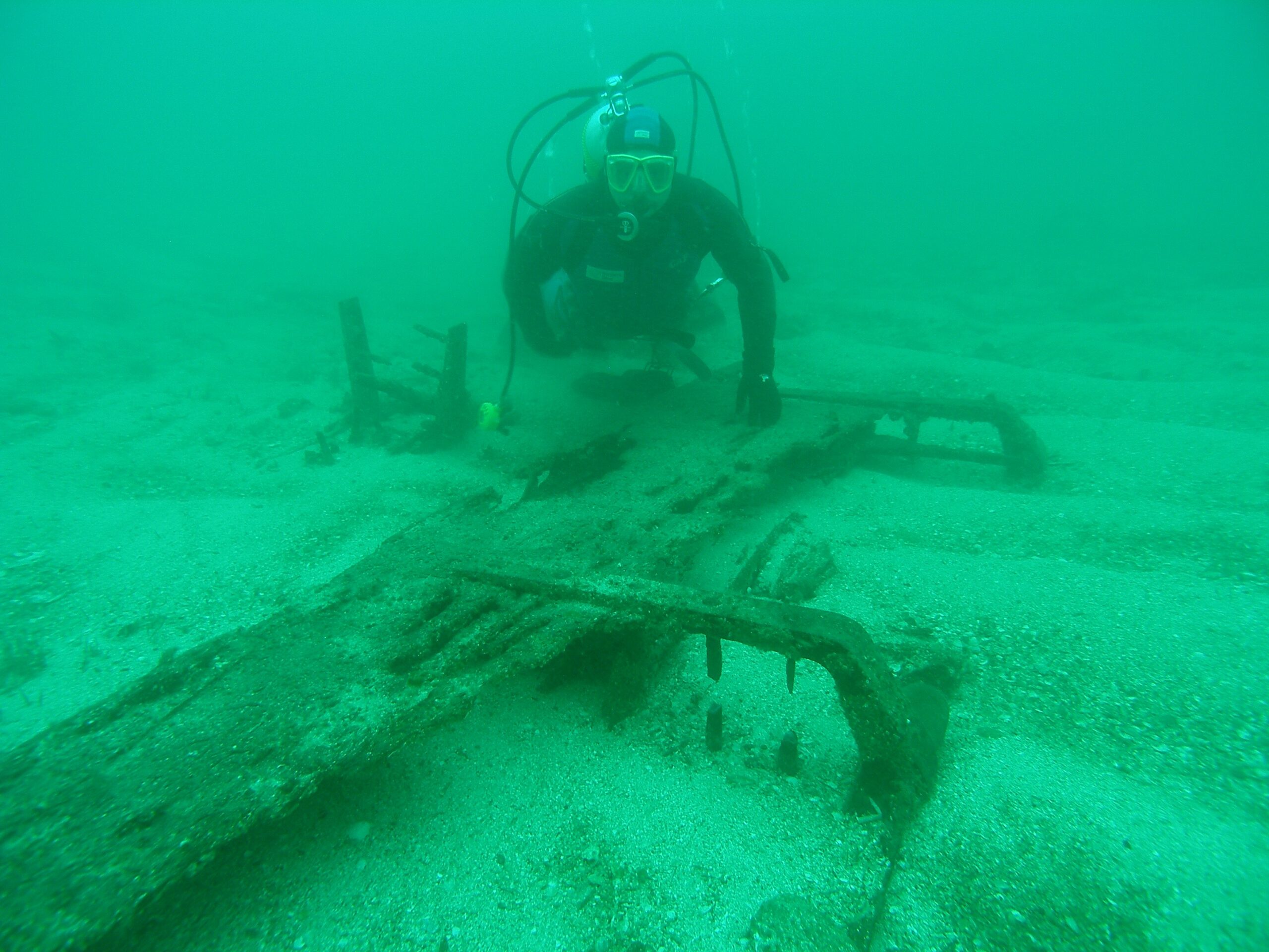 diver poses beside the Orpheus rudder resting on the sea floor.