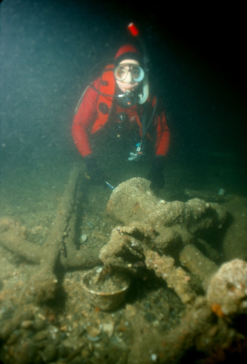 diver poses next to the Iroquois Windlass which is rusted over on the ocean floor