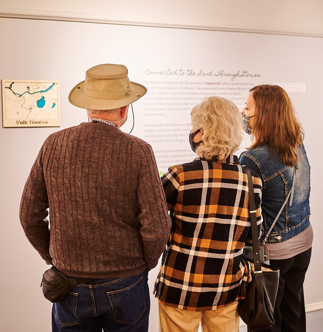 Inside Thretheway Exhibit opening, three adults stand and read a plaque in the exhibit