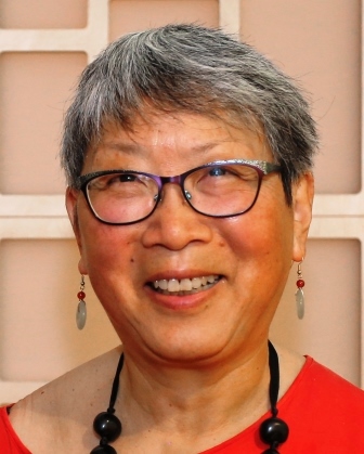 Middle Aged Chinese Canadian woman with grey hair wearing a red shirt, glasses, earrings and a beaded necklace