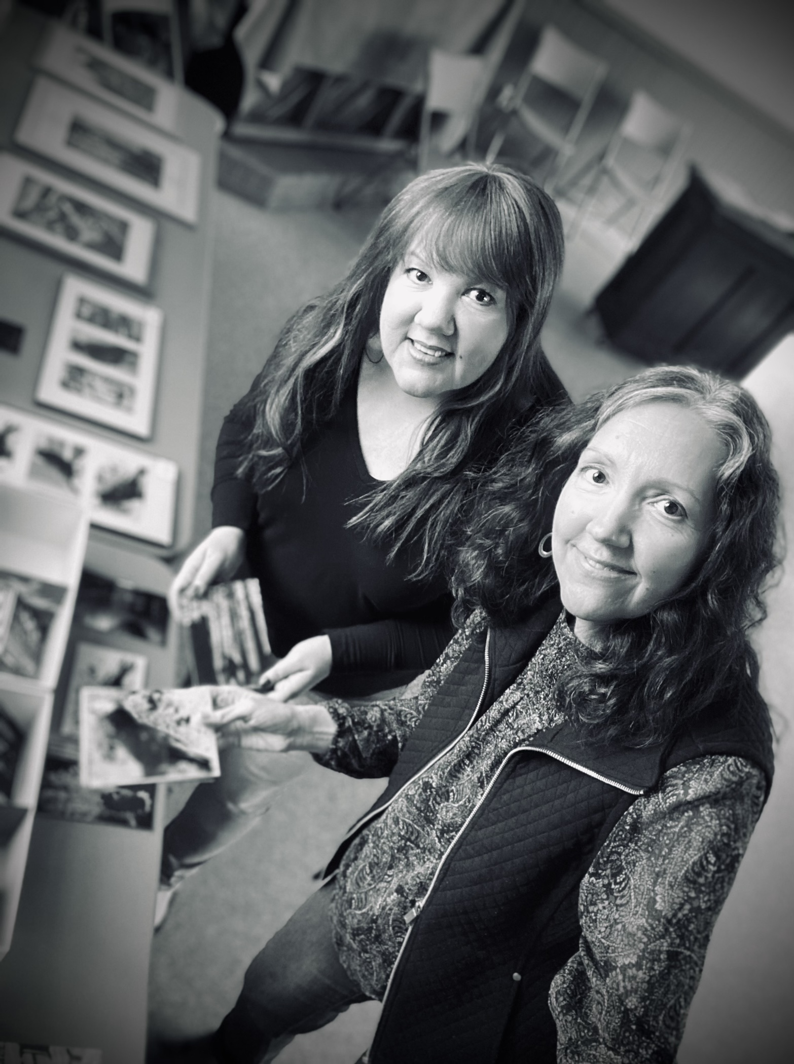 two women standing over a table with photographs laid out looking up at the camera smiling
