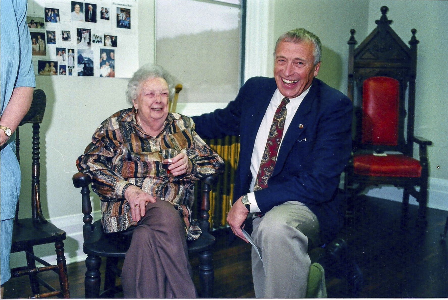 Ruby Nobbs in her 90s sitting on a chair with Mayor Dr. Geoff Battersby kneeling beside her at opening of Ruby Nobbs Community Archives