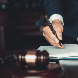 white man's hand holding a pen to sign documents with a judges gavel beside it