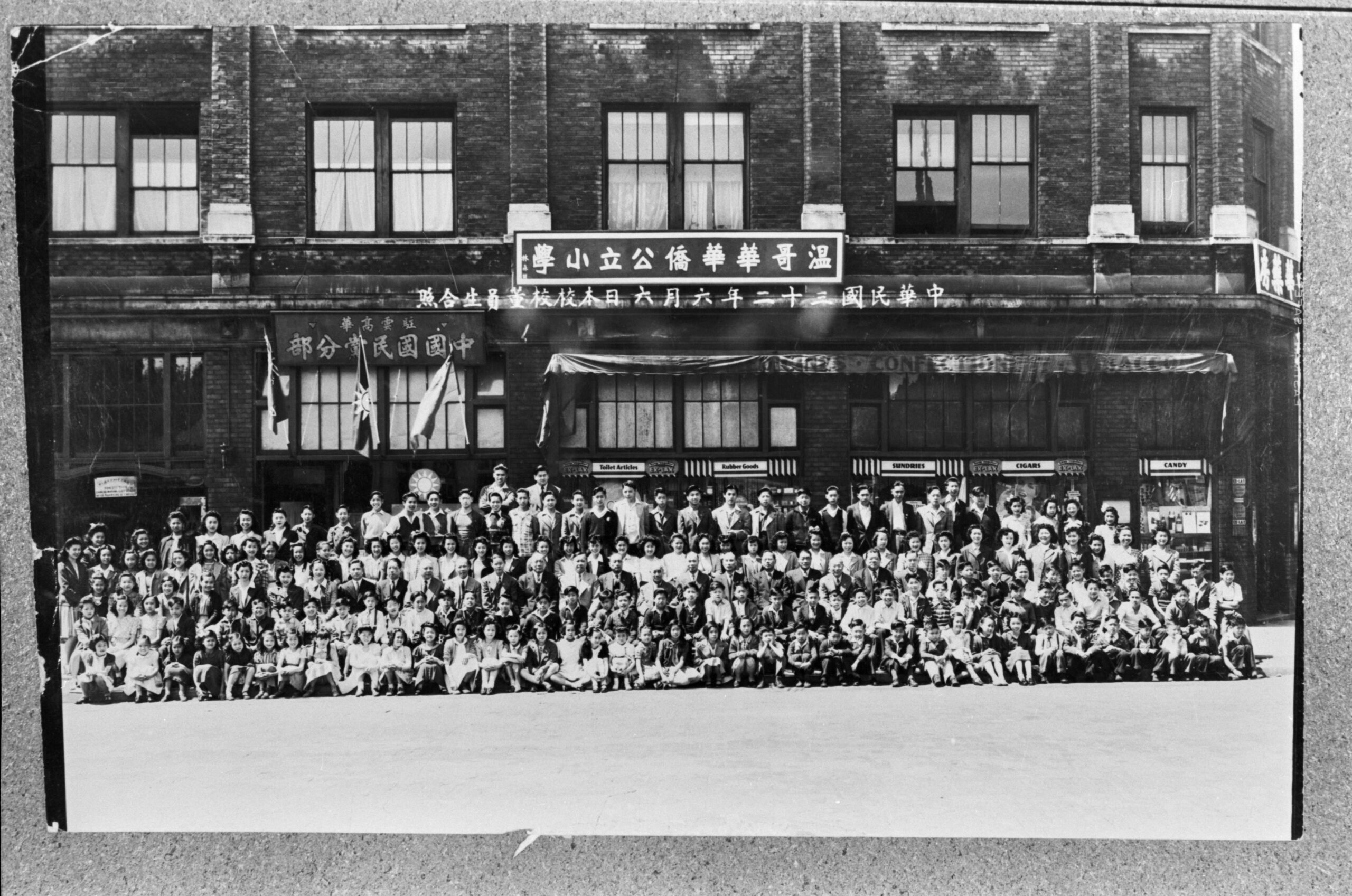 around 100 students pose in front of a large brick building with chinese characters on the front