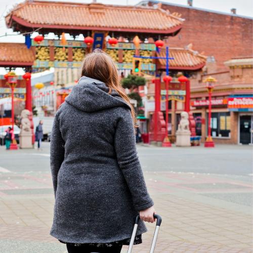 woman pulling a suitcase walking on a sidewalk towards a Chinese gate