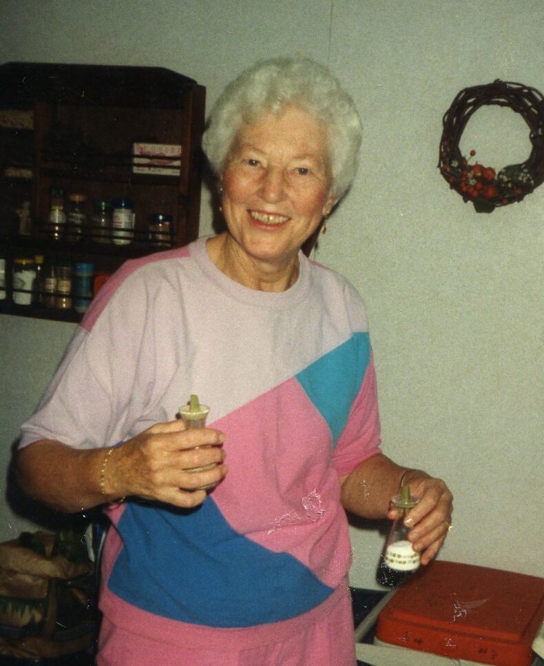 senior woman with short white curly hair in a pink and blue tee-shirt, inside with condiments in her hands.