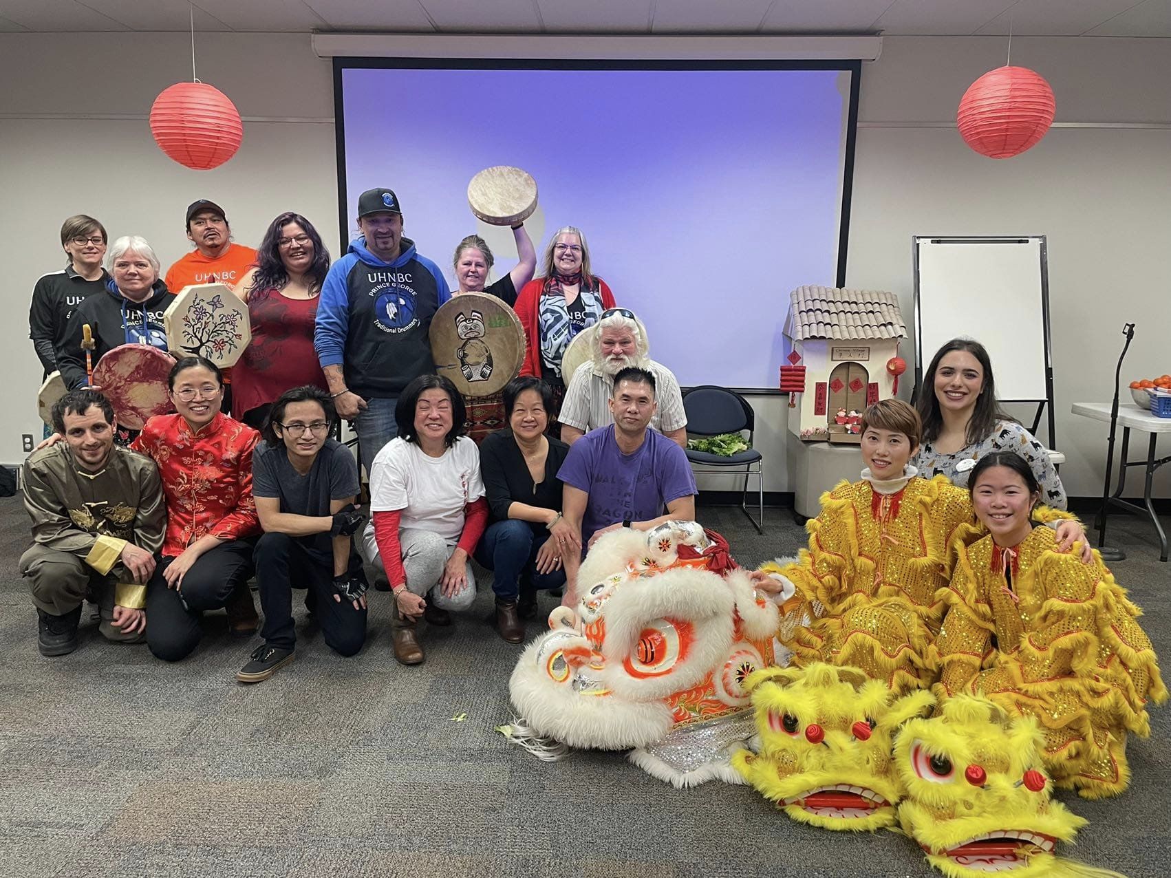 Lion dancers, drummers and organizers pose in front a screen and chinese new year lanterns
