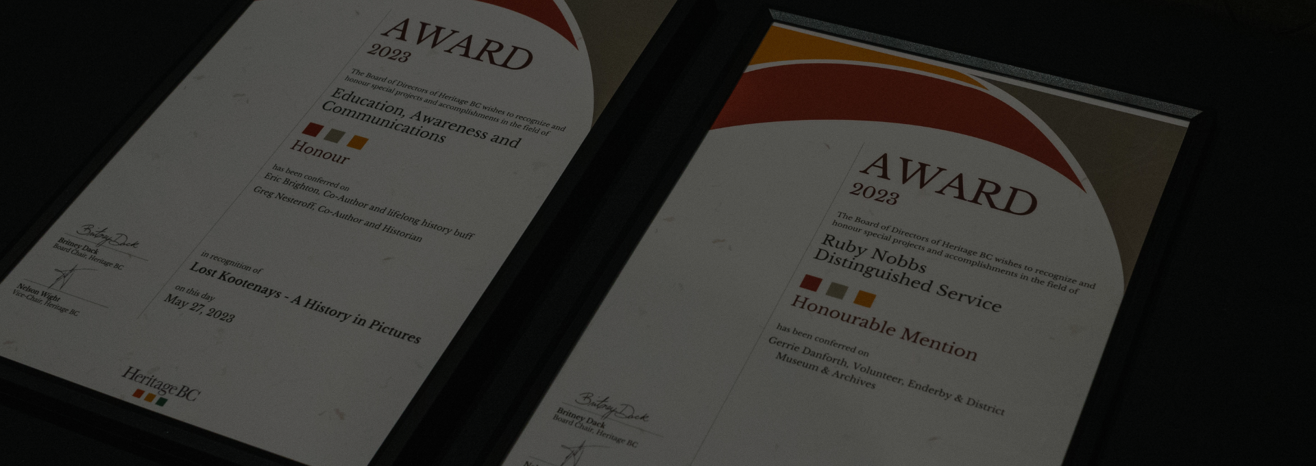Close up of two framed award certificates from 2023 on a black table